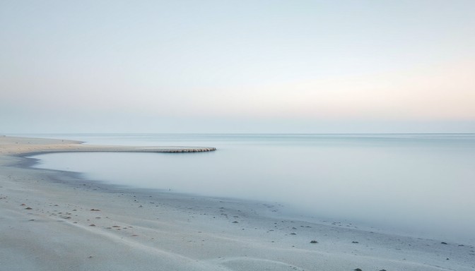 Stilla, ljus havsstrand i mjukt morgonljus